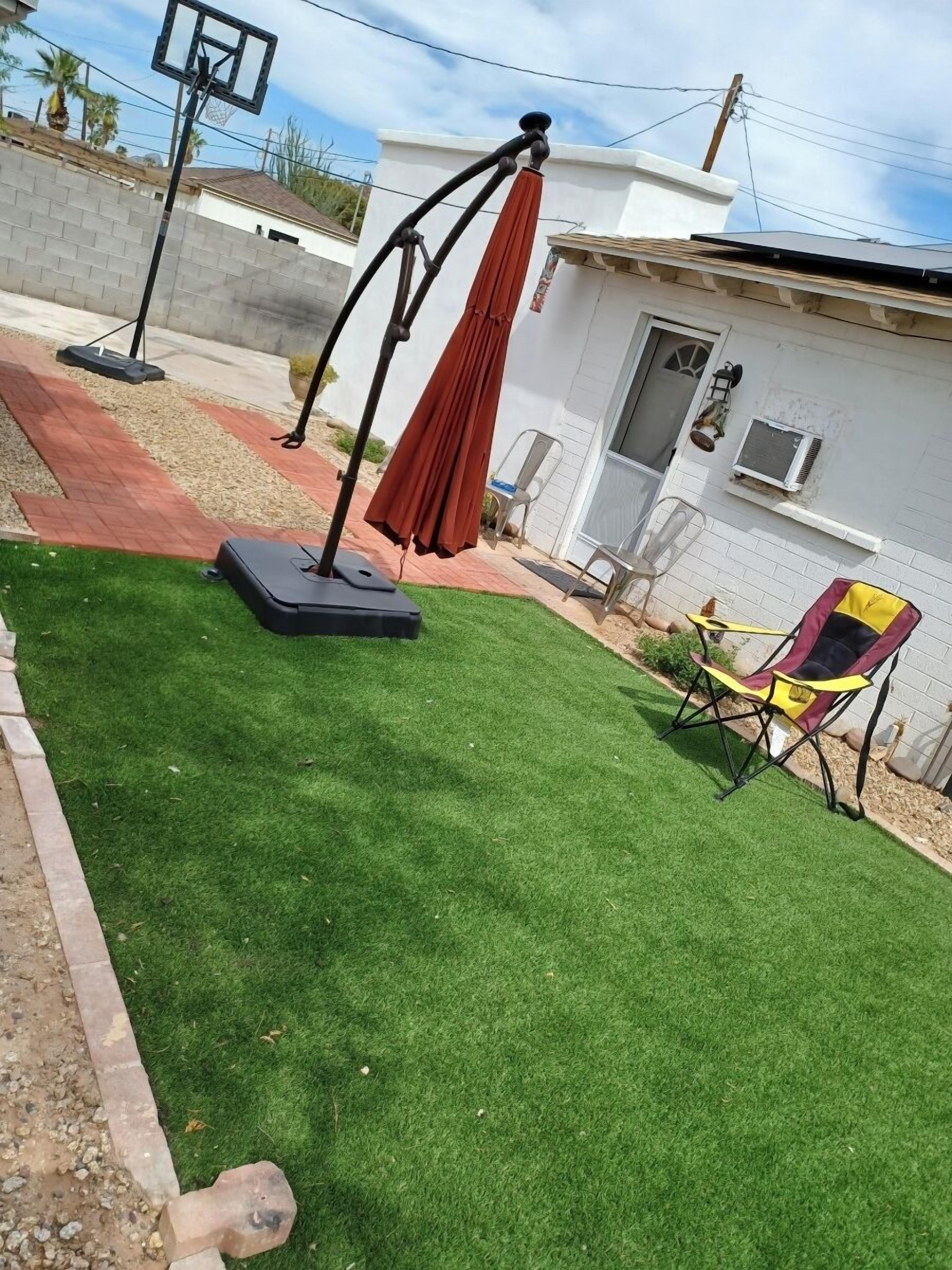 Un patio trasero con césped artificial, un columpio, una sombrilla y una silla plegable.