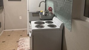 Een kleine keuken met een kookplaat, gootsteen en kastjes.