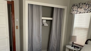 Una habitación de hotel con cama, mesita de noche, reloj y armario con cortinas.