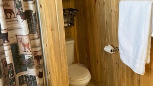 Un baño con paredes de madera, un inodoro, una cortina de ducha con estampados de animales y una toalla colgada en la pared.