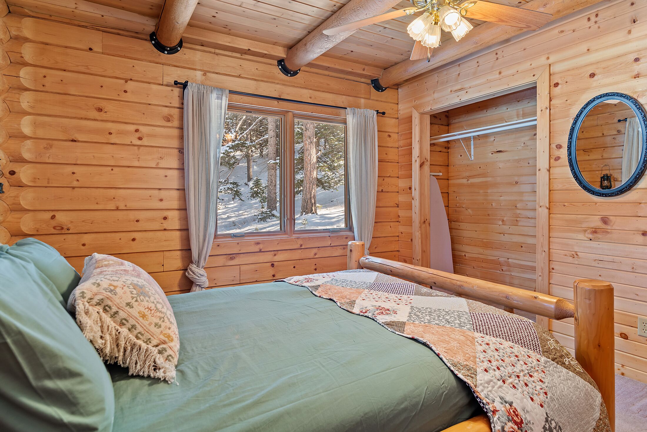 Una habitación de cabaña de madera con una cama, una ventana con cortinas y un espejo en la pared.