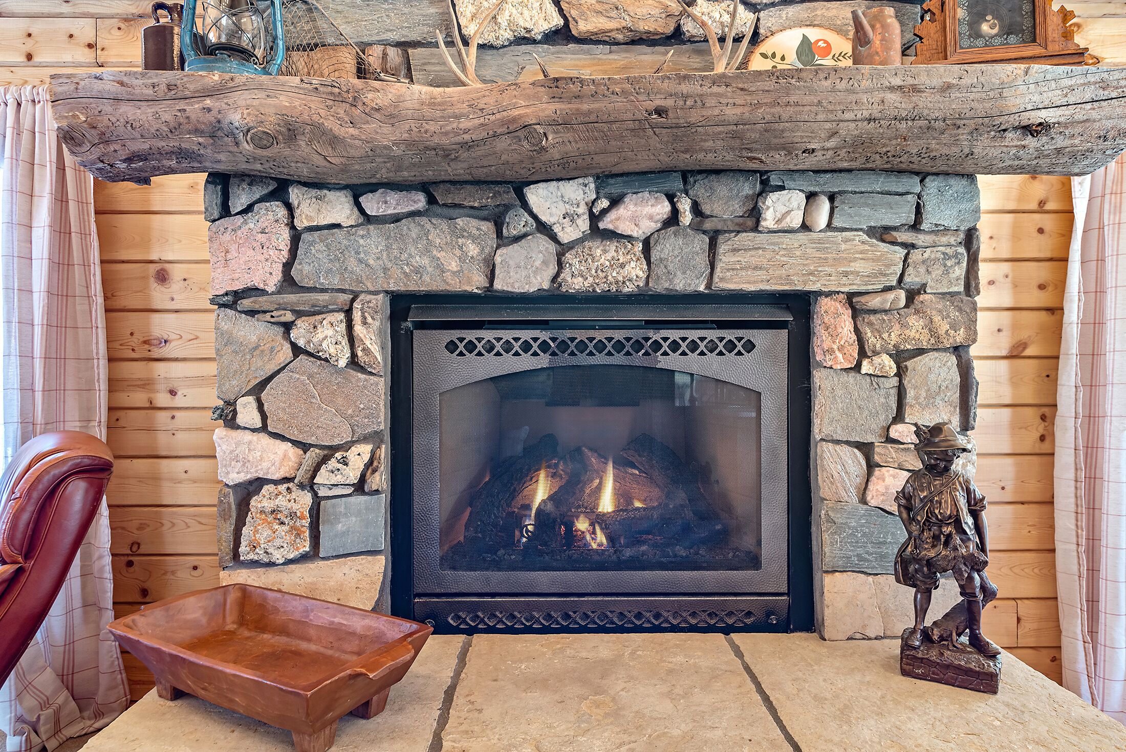 A stone fireplace with a log mantel, a wooden chair, and a small wooden tray.