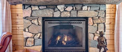 A stone fireplace with a log mantel, a wooden chair, and a small wooden tray.
