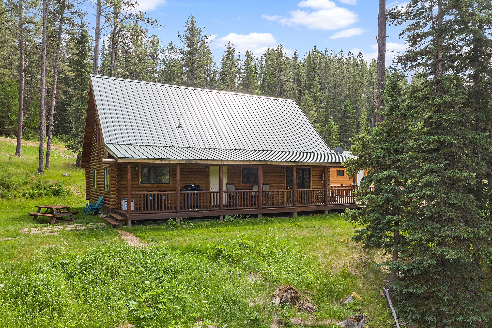 Une cabane en rondins avec un toit en métal, une véranda dotée de sièges d’extérieur et une table de pique-nique.