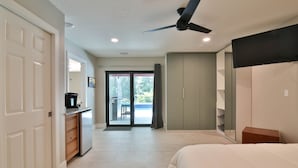 Ein Schlafzimmer mit Bett, Deckenventilator, Kleiderschrank und Blick ins Freie durch eine Glastür.