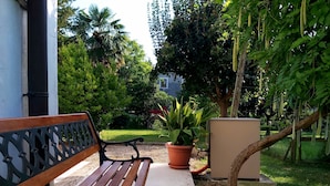 A bench with a metal frame and wooden slats, a potted plant, and a small structure, all set in a garden with trees and a building in the background. - "Da Celeste" Very bright apartment in a single house surrounded by greenery (Montegaldella)
