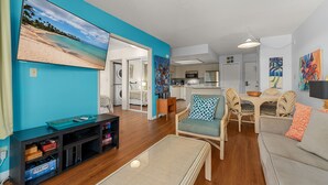 Ein Wohnzimmer mit großem Flachbildfernseher, einem Essbereich mit Tisch und Stühlen und einer Küche im Hintergrund.