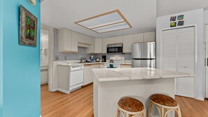 Eine moderne Küche mit weißen Schränken, einem Edelstahl-Kühlschrank und einer großen Kochinsel mit Sitzgelegenheiten.