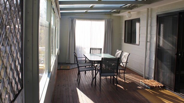 A sunlit room with a table and chairs, a sliding glass door, and a view of the outdoors. - Paradise Retreat (Paradise Beach)