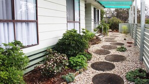 A house with a covered porch, a garden with various plants, and a pathway with stepping stones. - Paradise Retreat (Paradise Beach)