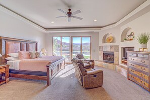 A bedroom with a large bed, a massage chair, a dresser, and a fireplace.