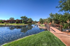A serene outdoor area with a pond, a wooden bridge, and a building with large windows.