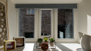 A room with a window, a clock, and three potted plants on a windowsill. - 23 Tanners Yard - Modern studio-style apartment in the heart of Kendal (Dog-friendly) (Kendal)
