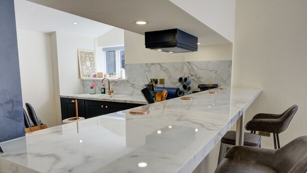 A modern kitchen with a marble countertop, a black range hood, and a large window. - 23 Tanners Yard - Modern studio-style apartment in the heart of Kendal (Dog-friendly) (Kendal)