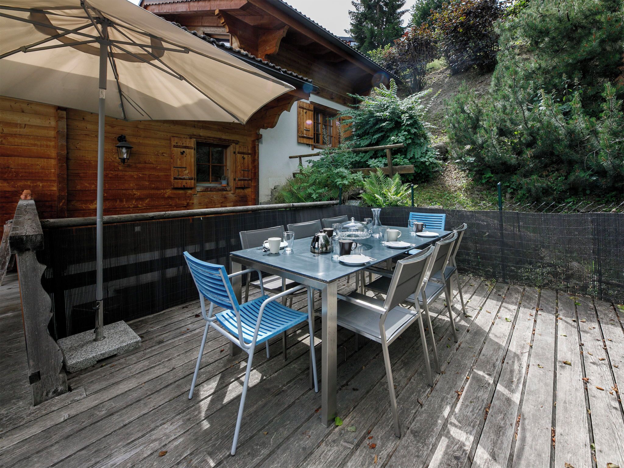Een terras met een eettafel voor vier personen, omringd door stoelen, met een grote parasol voor schaduw.