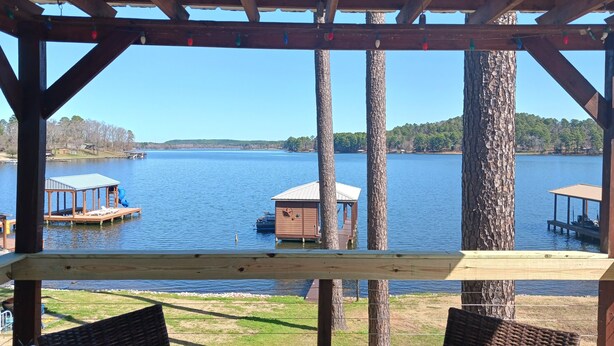 Una terraza de madera con sillas de mimbre que da vista a un lago, con muelles flotantes y una pequeña estructura de madera.
