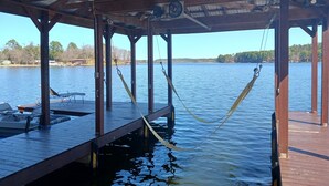 Un muelle de madera que se adentra en un lago tranquilo, con un espacio cubierto arriba y una hamaca atada entre los postes.