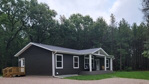 A single-story cabin with a porch, surrounded by a forest. - Beautiful new house 5 min from Sand Valley Golf and 45 min from Wisconsin Dells  (Nekoosa)