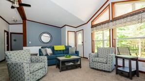 A living room with two patterned armchairs, a blue sofa, a coffee table, and a window with a view of greenery. - Beautiful new house 5 min from Sand Valley Golf and 45 min from Wisconsin Dells  (Nekoosa)