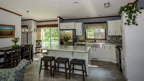 A kitchen with a central island, white cabinets, a dining area with a patterned sofa, and a painting on the wall. - Beautiful new house 5 min from Sand Valley Golf and 45 min from Wisconsin Dells  (Nekoosa)
