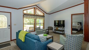 A living room with a blue sofa, patterned armchairs, a small table, a TV, and a large window with curtains. - Beautiful new house 5 min from Sand Valley Golf and 45 min from Wisconsin Dells  (Nekoosa)