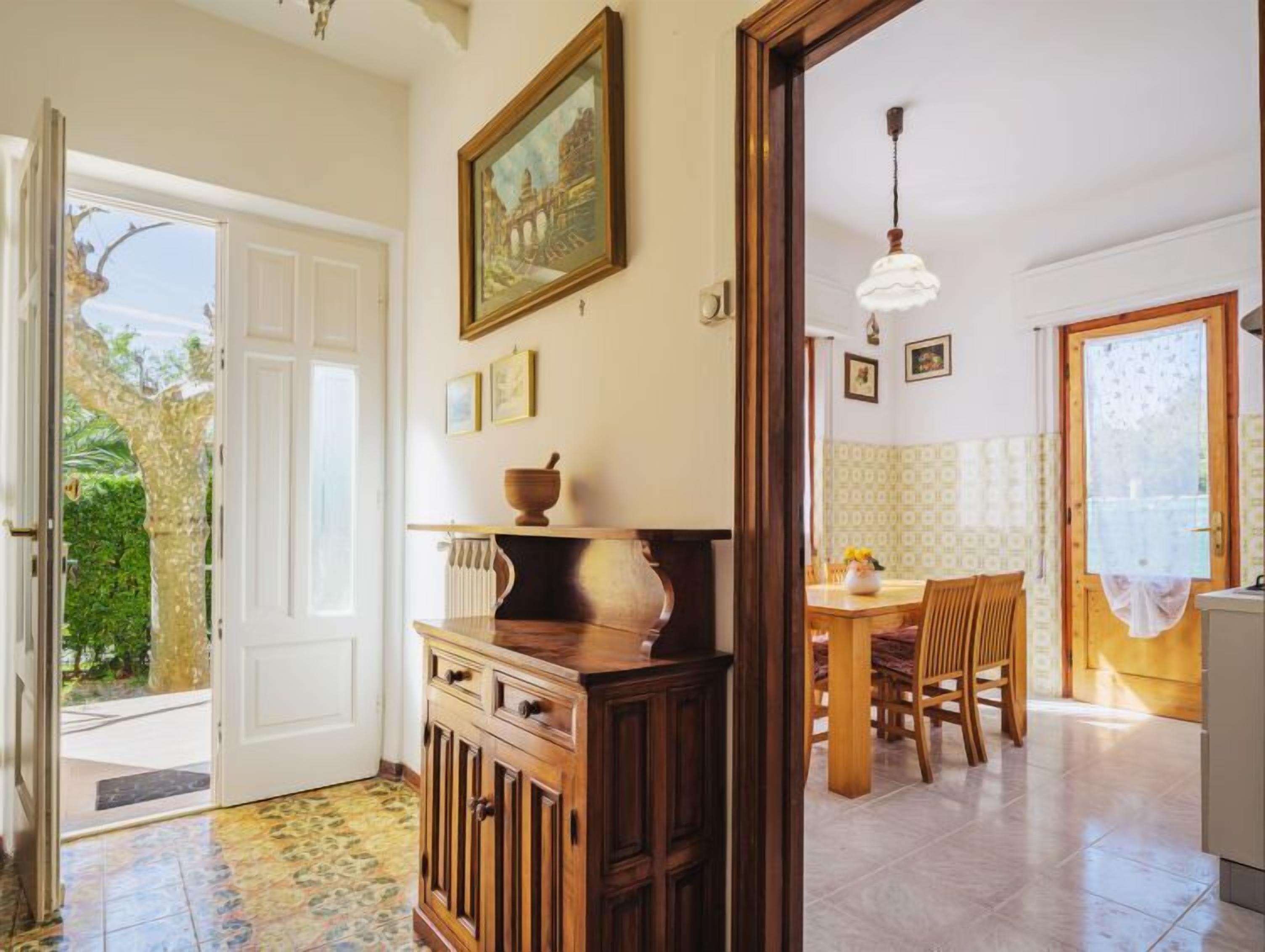 A room with a wooden cabinet, a painting, a dining table with chairs, and a view of the outside.