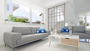 Ein modernes Wohnzimmer mit zwei grauen Sofas, einem weißen Couchtisch und einem großen Fenster mit Blick auf Gebäude und Grünflächen.
