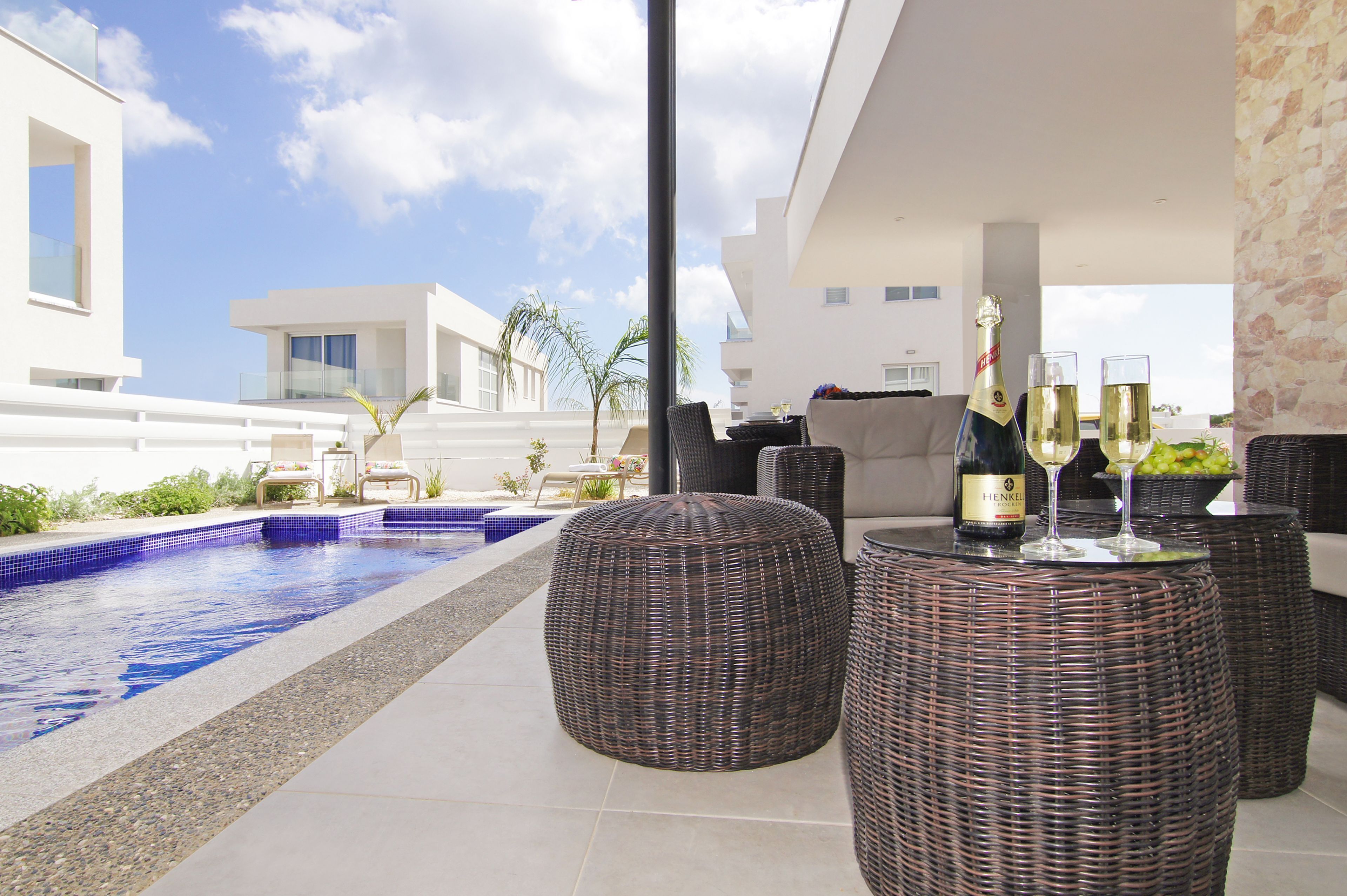 A modern outdoor pool area with wicker furniture and a bottle of champagne.