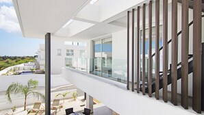 Ein moderner Balkon im Freien mit Glasgeländer, Pool und Essbereich mit Stühlen und Tischen.