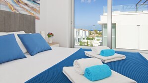 Ein modernes Hotelzimmer mit einem großen Bett, blauer Bettwäsche und Blick auf die Küste.