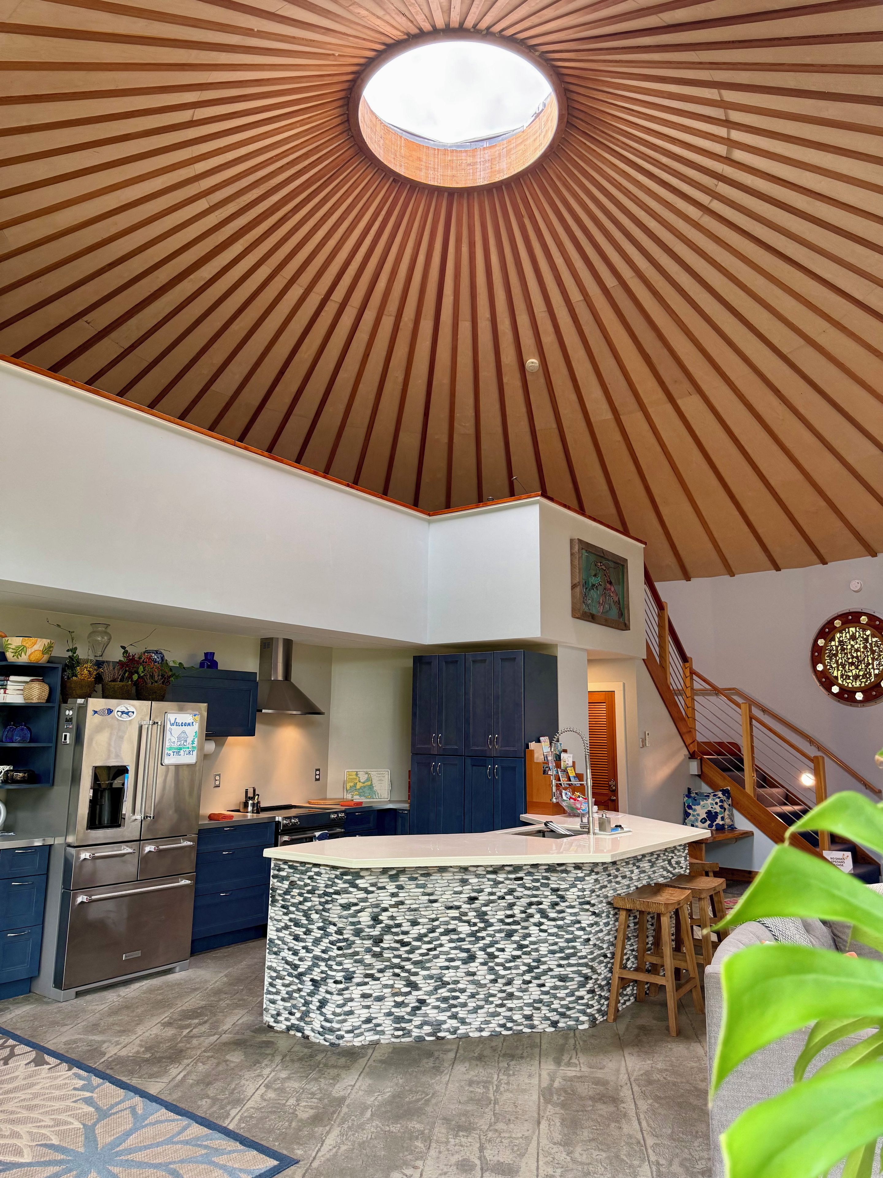 Une cuisine moderne dotée d’un îlot central, d’un plafond en bois et d’un escalier menant à un autre niveau.