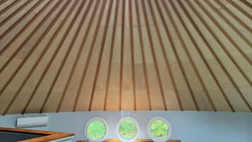 A circular skylight with wooden beams radiating inward, a white air conditioning unit, and three circular windows with greenery views.
