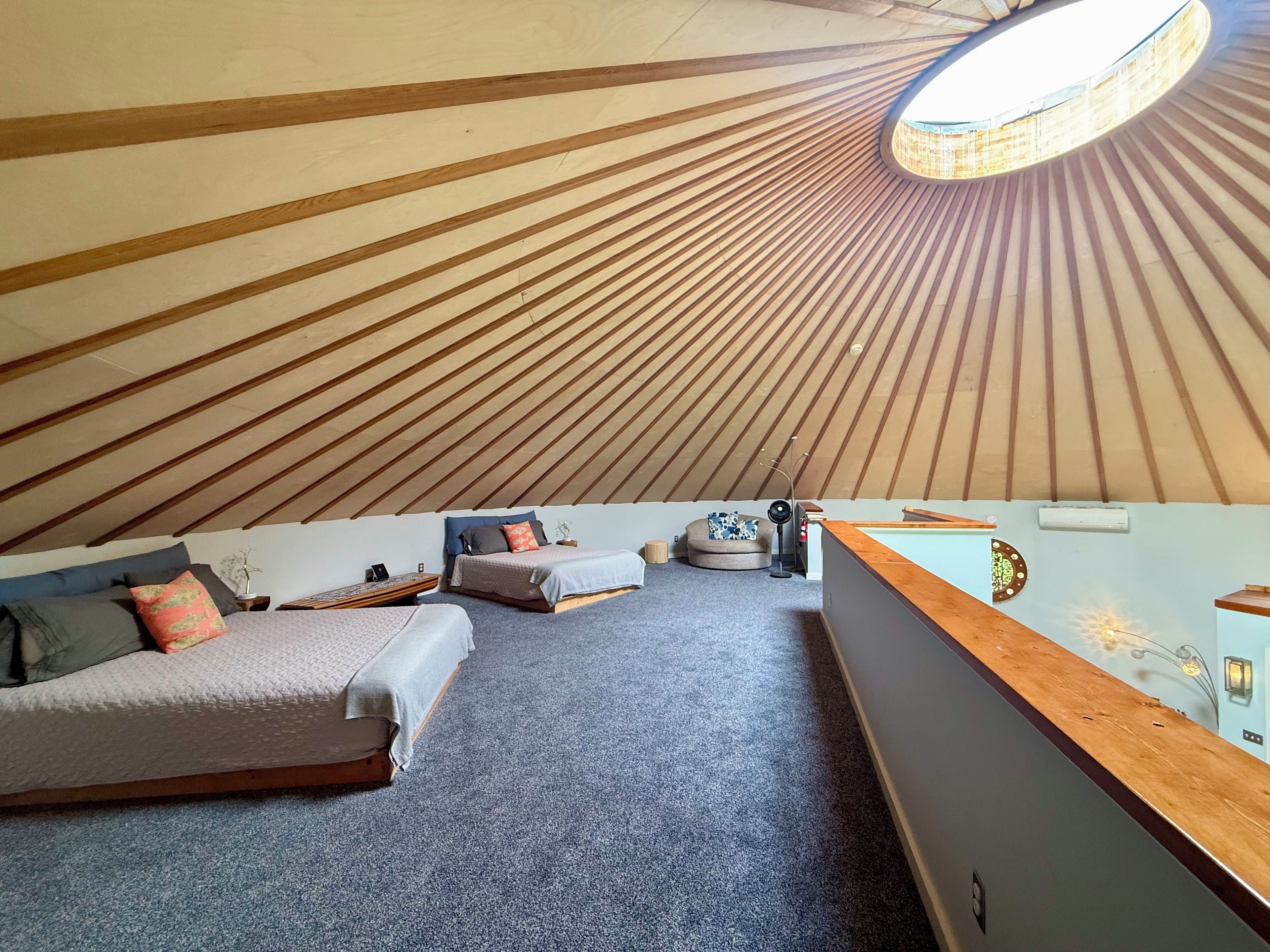 A room with a sloped ceiling, a bed, a sofa, a small table, and a wall-mounted light fixture.
