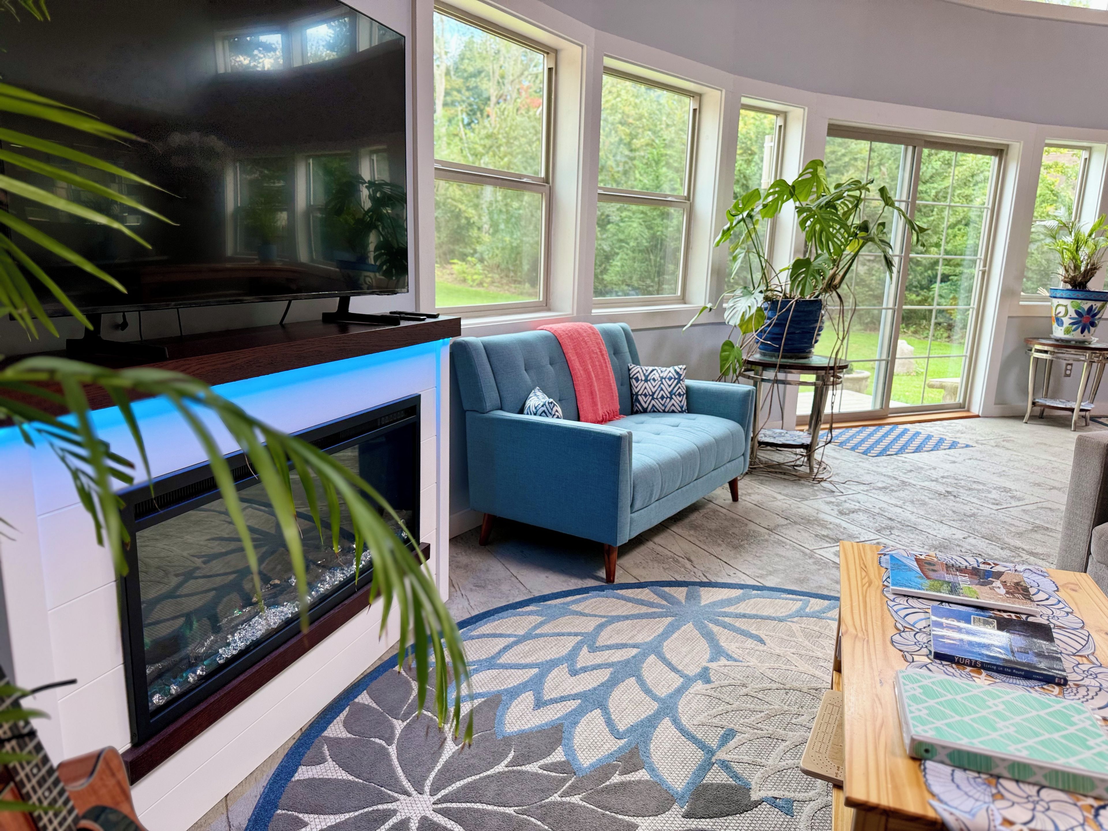A living room with a fireplace, a sofa, a television, and a large window overlooking greenery.