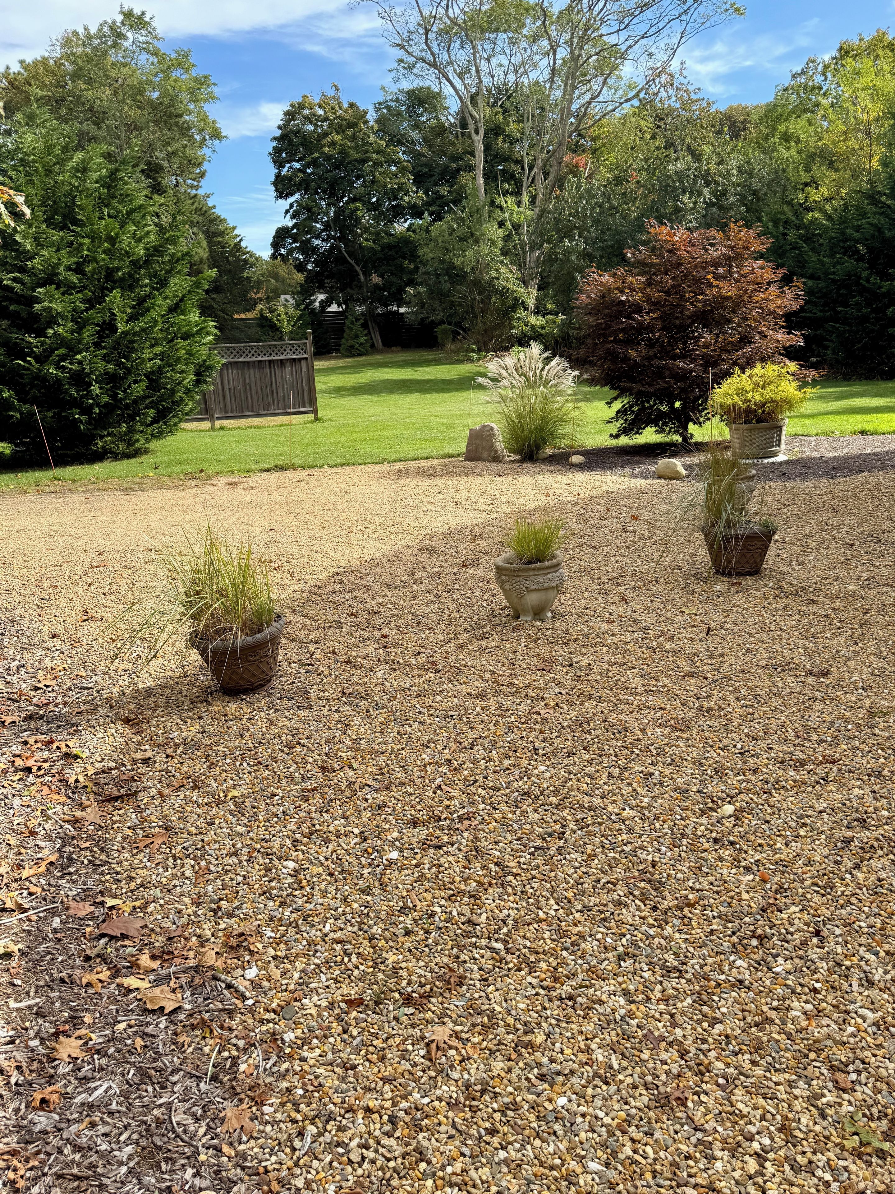 Un jardín con suelo de grava, plantas en macetas y una cerca de madera al fondo.