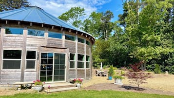 A wooden building with a curved roof and large windows, surrounded by a well-maintained garden with various plants and a patio area.