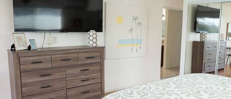 Un dormitorio con cama, cómoda, televisor montado en la pared y un cuadro.