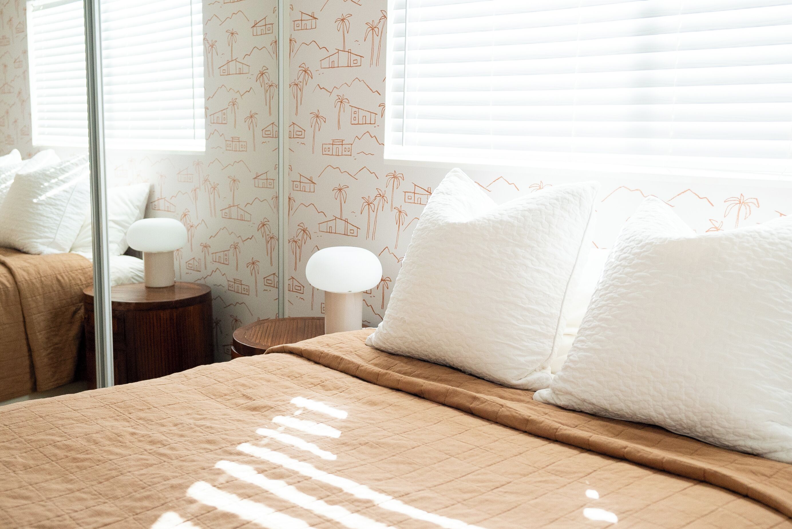 A neatly made bed with a brown quilt, white pillows, and a bedside lamp on a wooden nightstand.