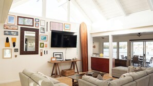 Un salon spacieux avec un plafond haut, un grand téléviseur à écran plat et une planche de surf en bois.