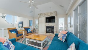 A spacious living room with a fireplace, blue sofas, wicker chairs, and a ceiling fan. - 1623 - Breakaway - Bring the Pup! Corolla Escape w/ Pool & Hot Tub (Corolla)