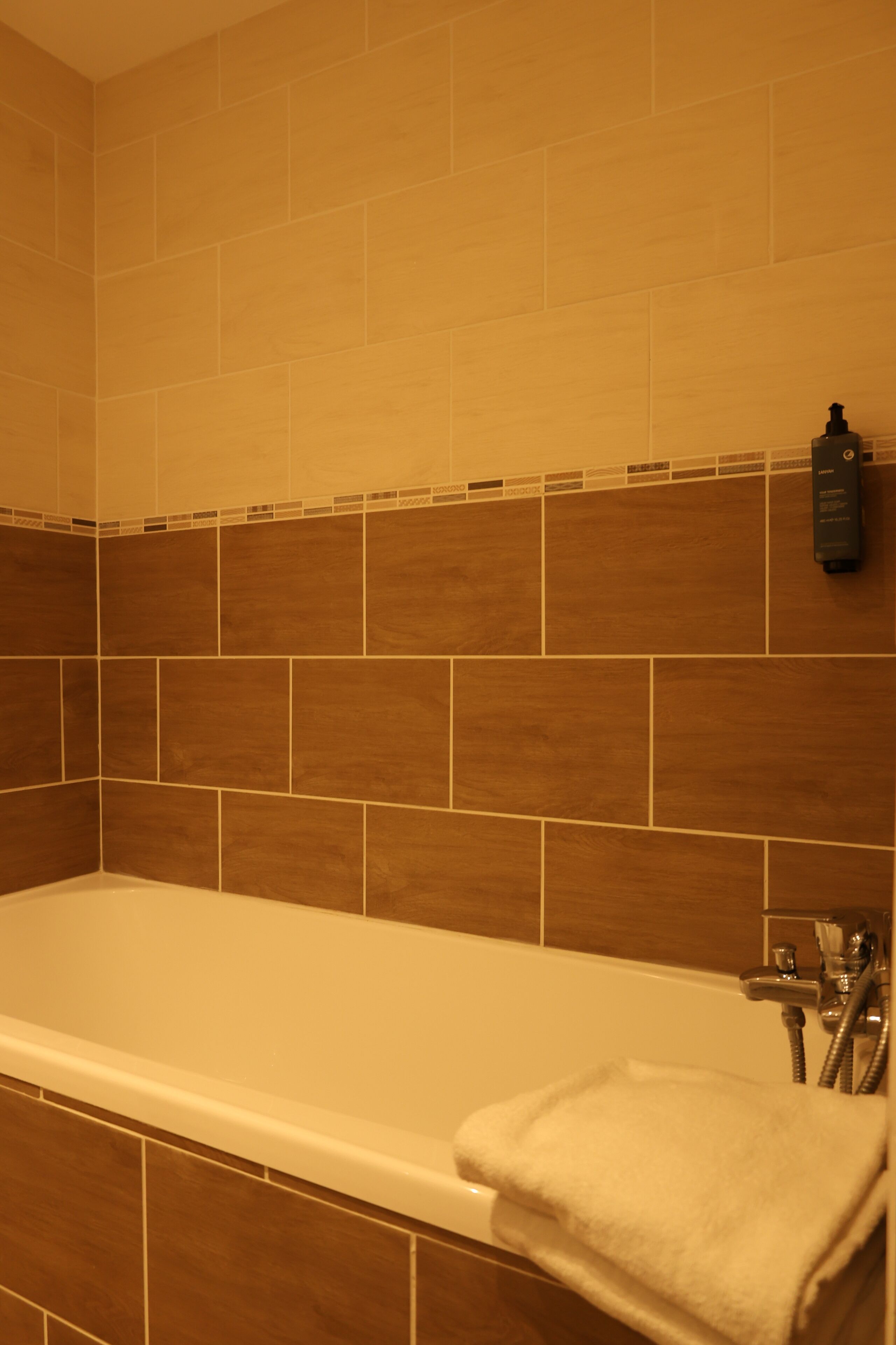 Un baño con bañera, una toalla y un dispensador de jabón en la pared.