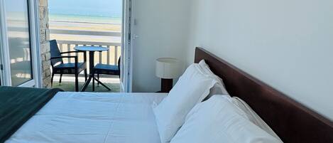 Una camera d'albergo con un letto, vista sulla spiaggia e un tavolo con sedie all'esterno.