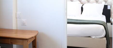 A bedroom with a tufted headboard, a bed with white bedding, a wooden desk, and a framed picture on the wall.