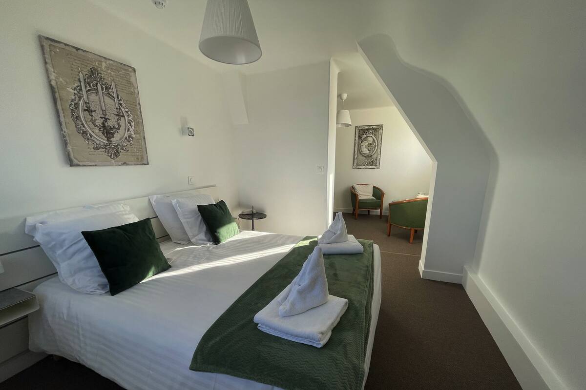 A hotel room with a bed, a chair, a small table, and a painting on the wall.