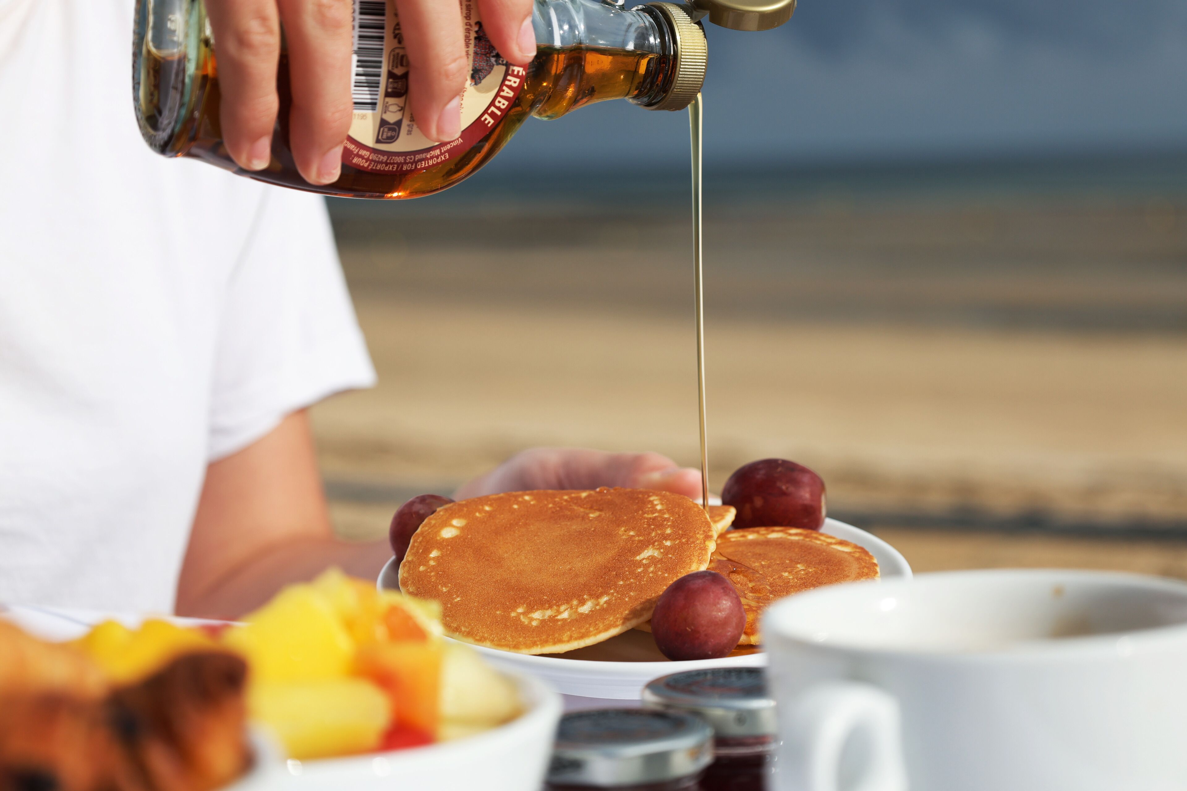 Sirup wird auf Pfannkuchen mit Obst auf einem Tisch gegossen.