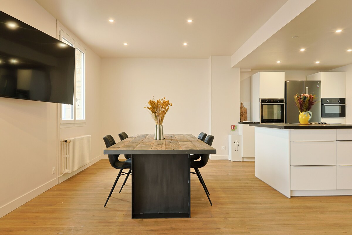 Eine moderne Küche mit integrierten Geräten, ein Essbereich mit Holztisch und -stühlen sowie eine zentrale Vase mit Trockenblumen.