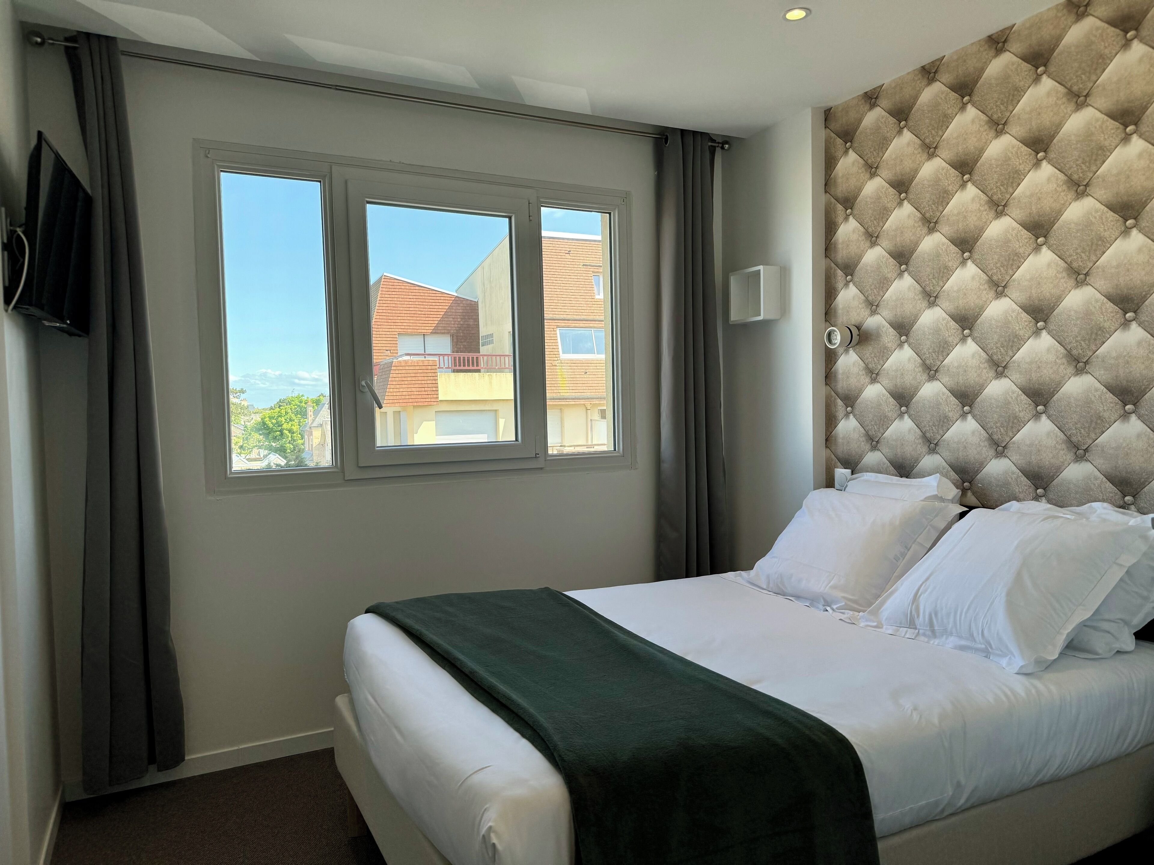 A hotel room with a bed, a window, a television, and a tufted headboard.