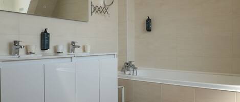 A modern bathroom with a white vanity, a large mirror, and a bathtub.