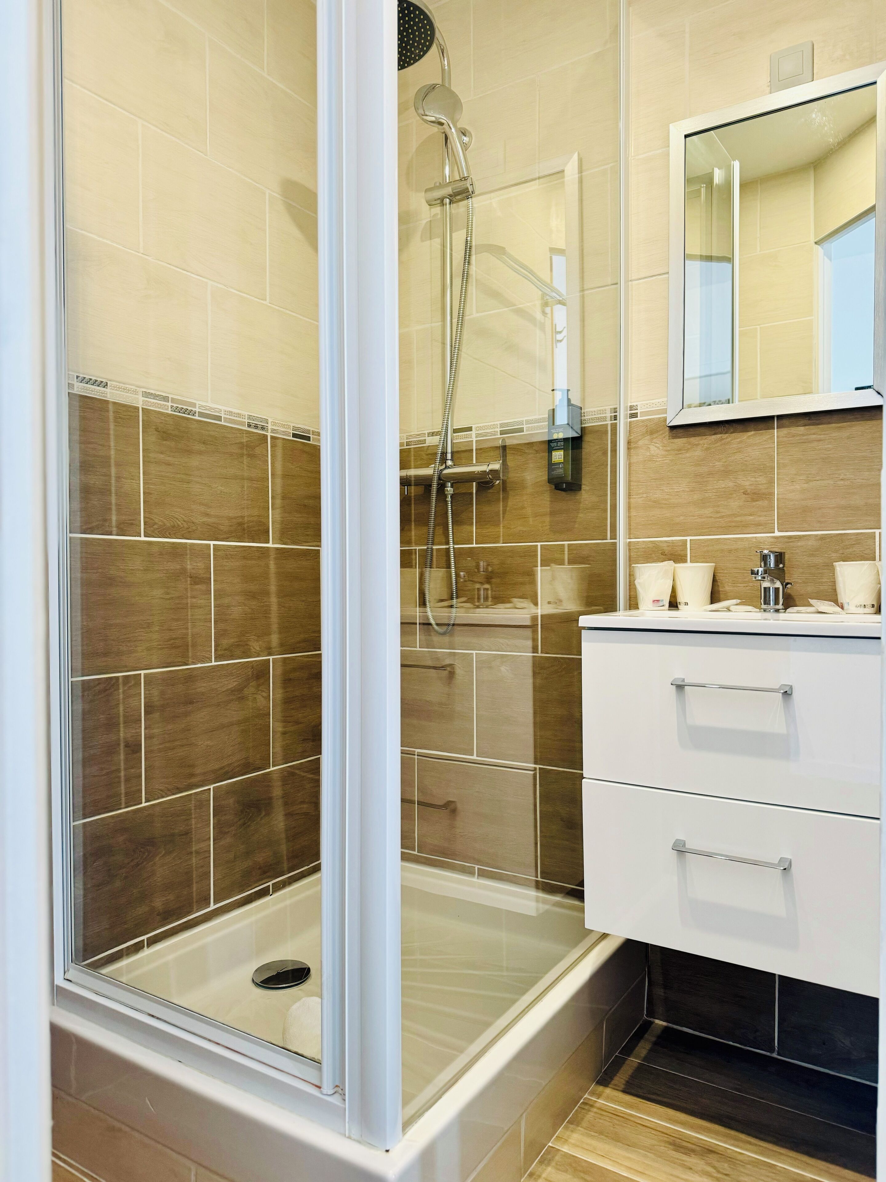 A modern bathroom with a glass-enclosed shower, beige tiles, and a white vanity with drawers.