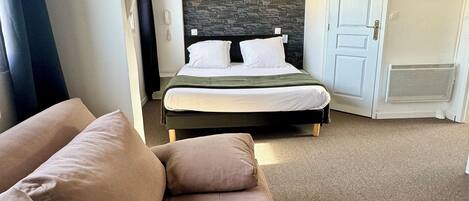 A modern hotel room with a large bed, a built-in headboard, a dark stone accent wall, a white door, and a beige carpet.